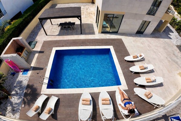 A rooftop pool with a square shape, surrounded by lounge chairs and a table.