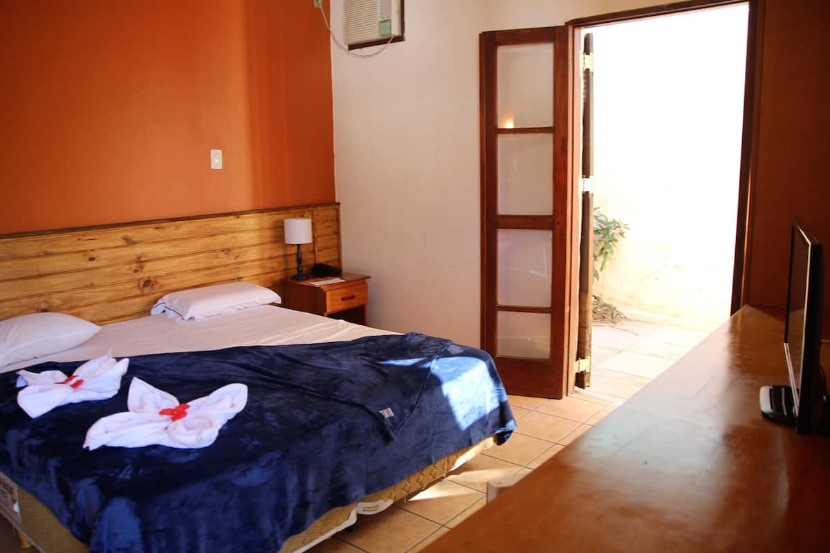 A hotel room with a bed, a nightstand, a TV, and a sliding glass door leading to a balcony.