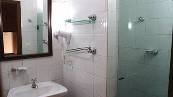 A bathroom with a white sink, a mirror, a hairdryer, and a shower with a glass shelf.
