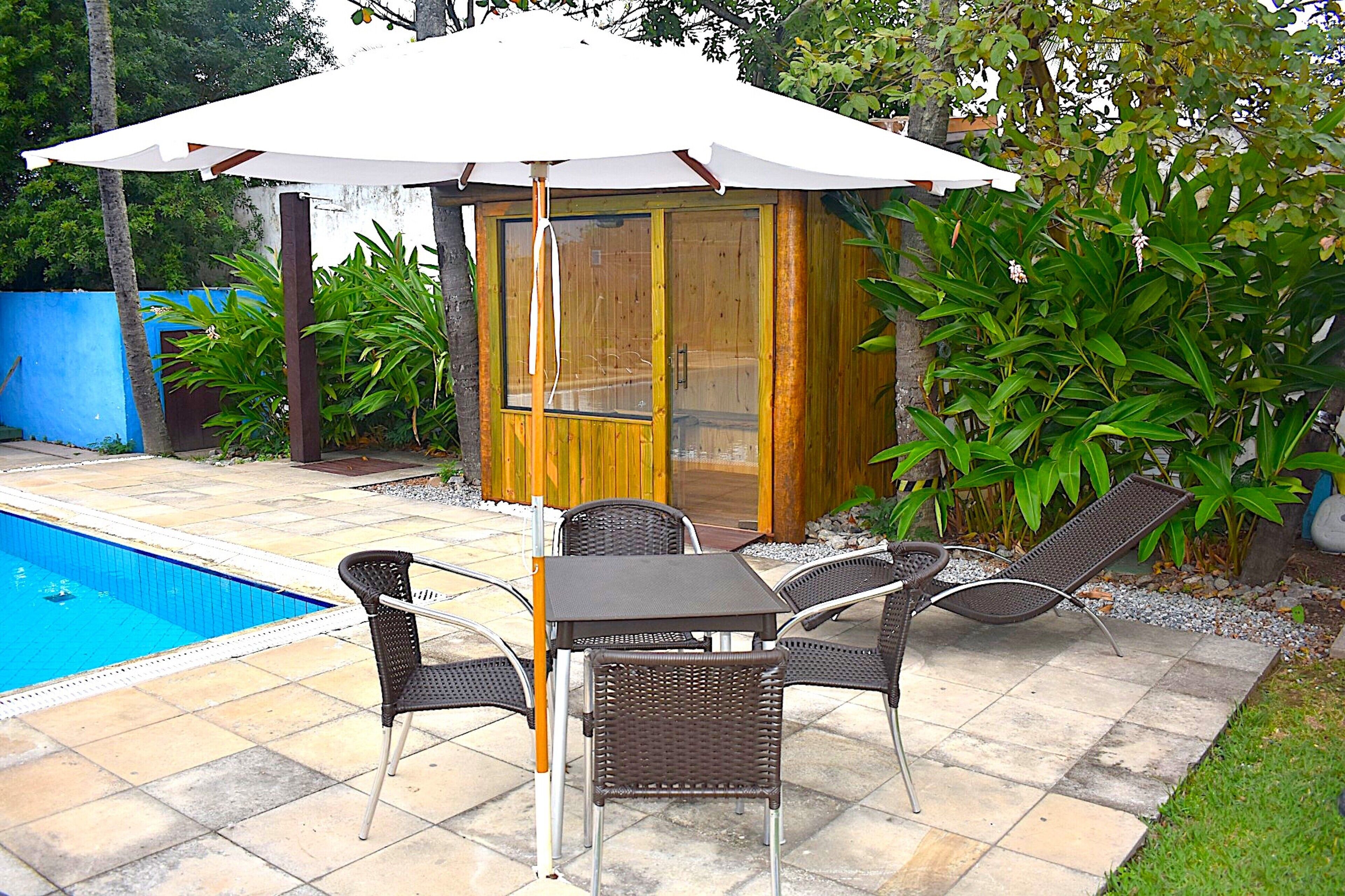 A poolside area with a wooden structure, a table, and chairs under a white umbrella.