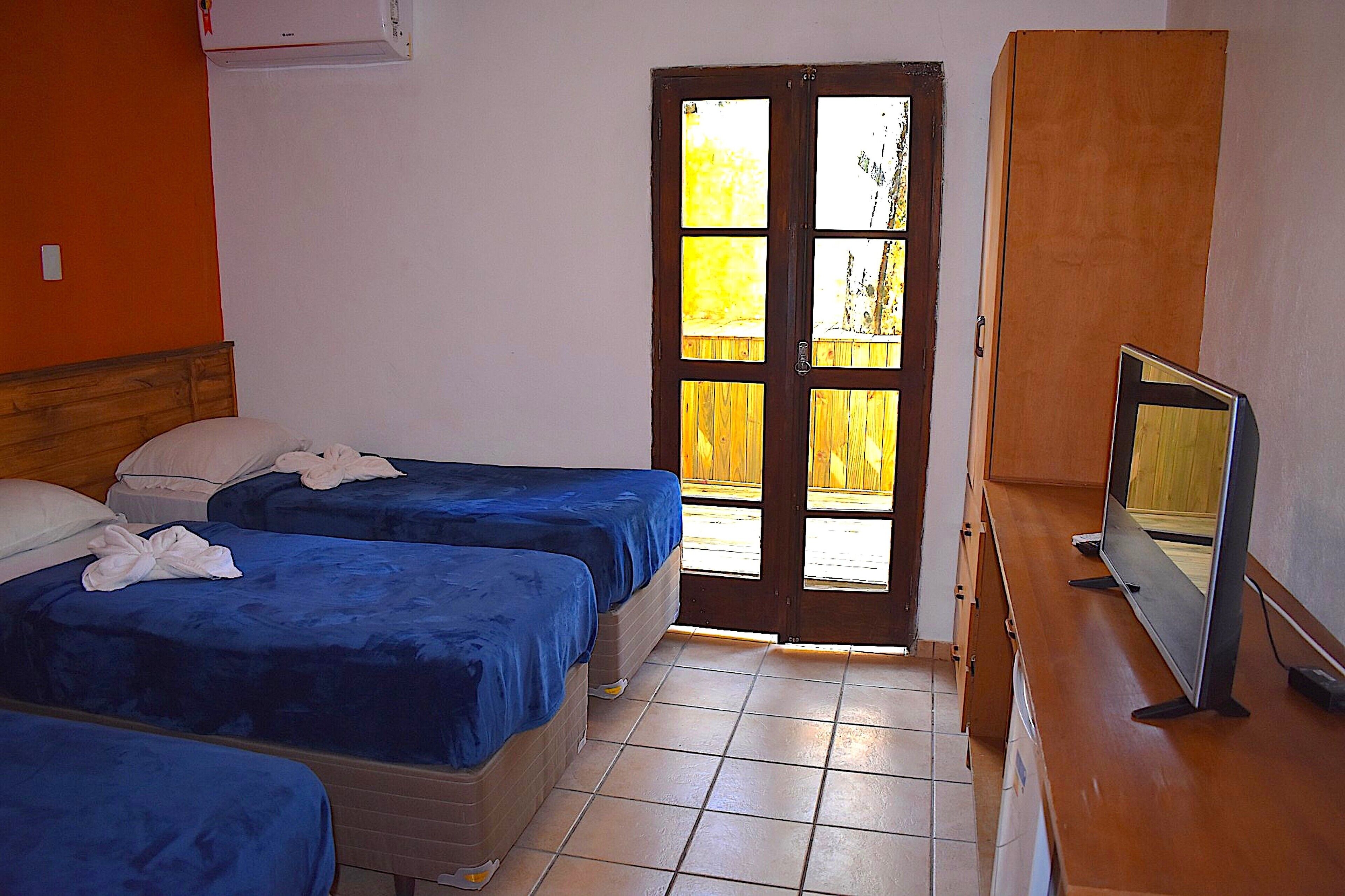 A room with three beds, a television, and a wooden wardrobe.