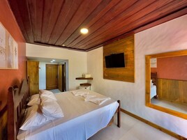 Een hotelkamer met een houten plafond, een bed met witte lakens, een wandtelevisie en een spiegel aan de muur.