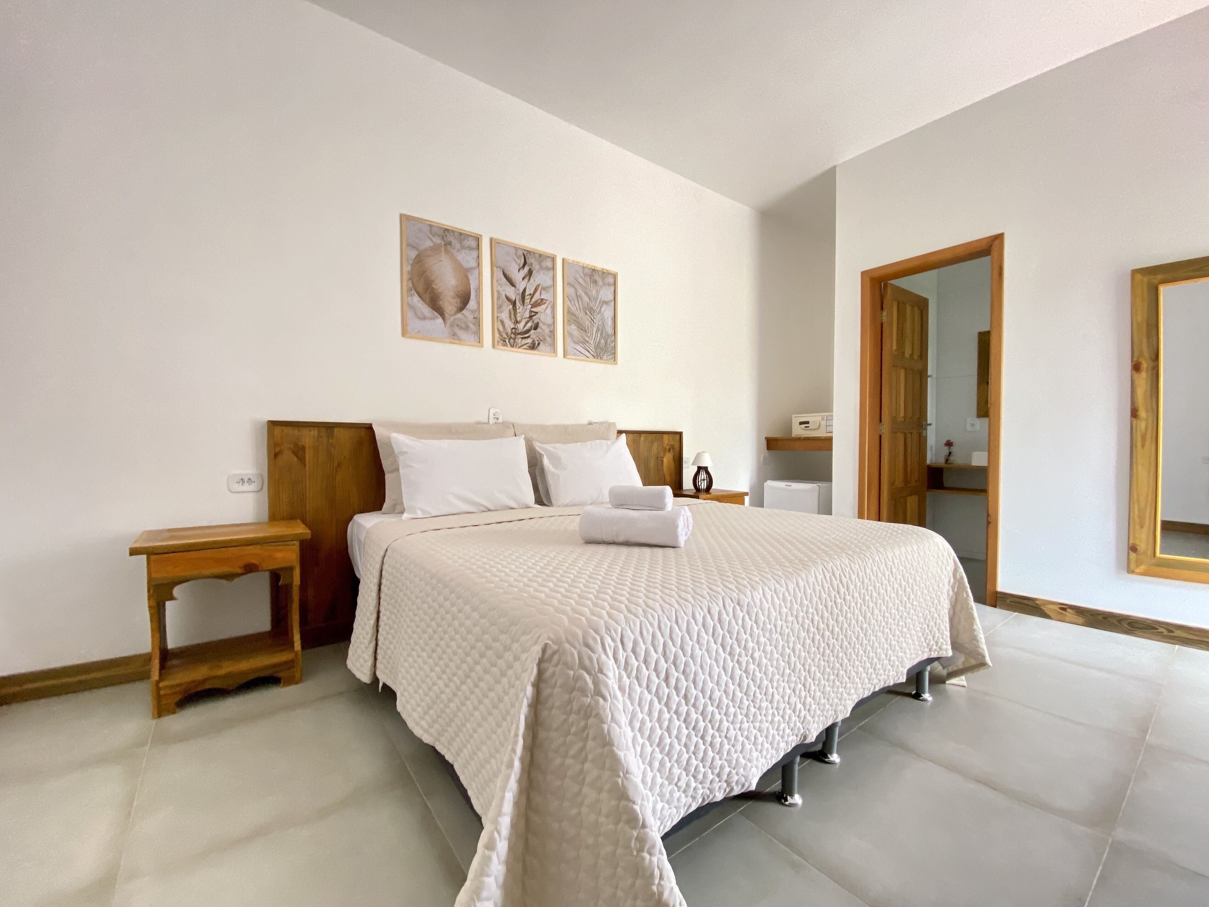 A neatly arranged bedroom with a large bed, wooden headboard, bedside tables, and a mirror.