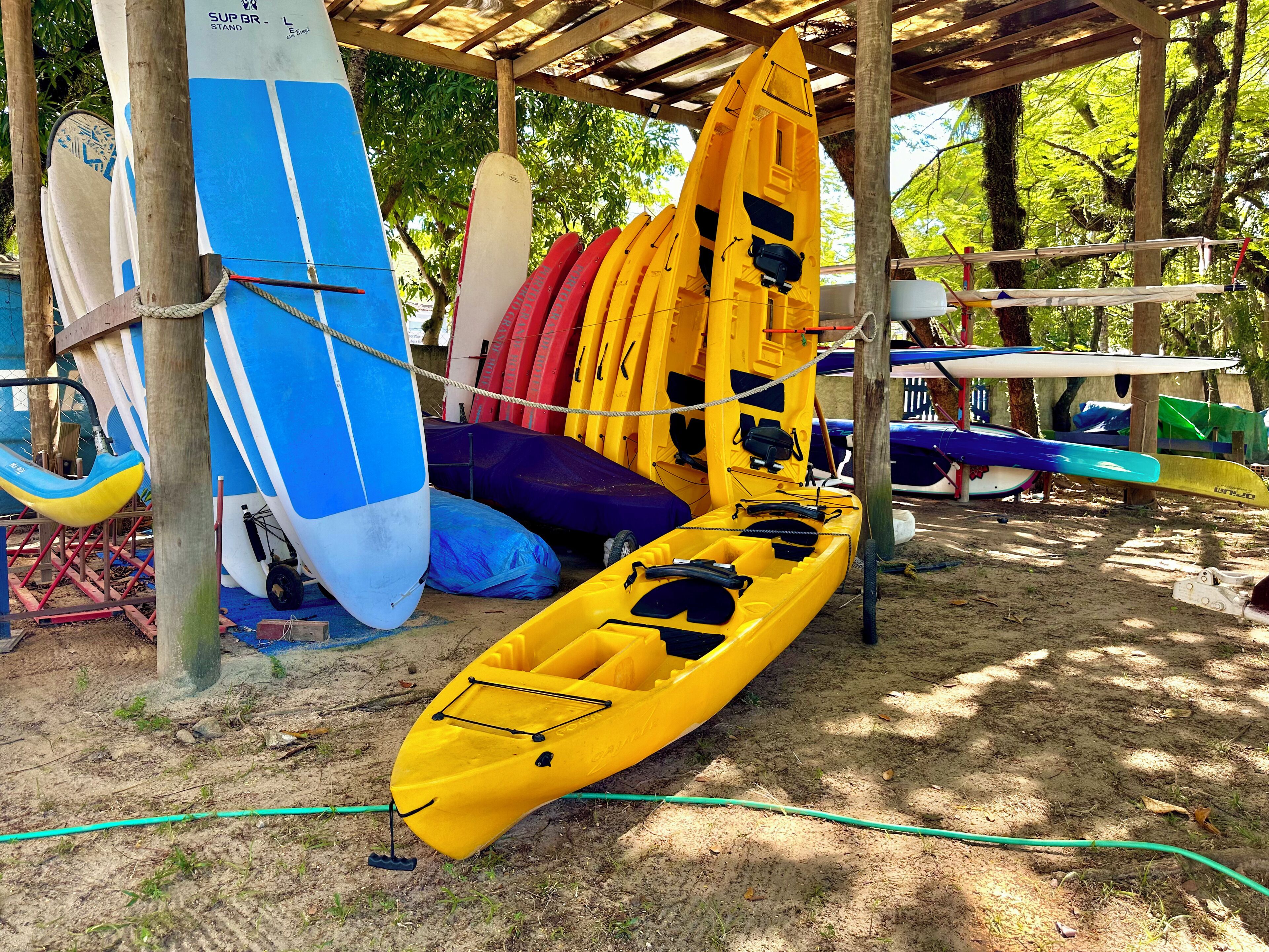 A covered area with various kayaks and a surfboard.