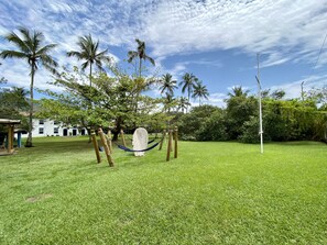 A grassy outdoor area with a hammock, palm trees, and a building in the background. - Porto Grande Hotel & Convention (São Sebastião)