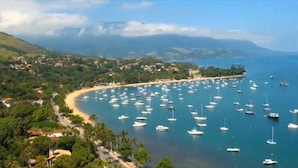 A coastal town with a beach, numerous boats, and lush greenery. - Porto Grande Hotel & Convention (São Sebastião)