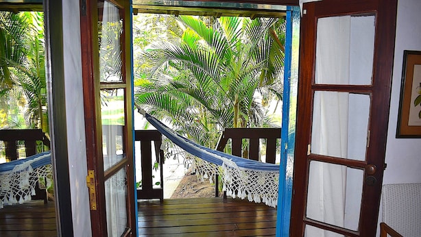 A wooden deck with a hammock and a view of palm trees. - Porto Grande Hotel & Convention (São Sebastião)