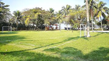 A grassy field with a playground, palm trees, and a soccer goal.