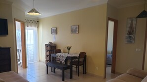 Een woonkamer met een bank, een eettafel met stoelen en een aan de muur bevestigde televisie.