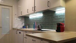 Eine K üche mit weißen Schränken, einer Edelstahl-Dunstesse, einer gefliesten Spritzschutzwand und einer Arbeitsplatte mit Wasserkocher und einem roten Gerät.