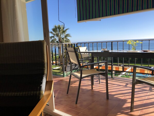 Un balcón con una mesa y sillas, con vistas a una piscina y palmeras.