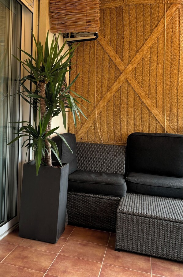 Esquina de una habitación con un sofá negro, una planta en maceta y un panel de pared tejido.
