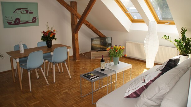 A cozy living room with a wooden floor, a white sofa, a dining table with chairs, a TV, and a window with a view of trees. - Chickes apartment in perfect location (Graz)