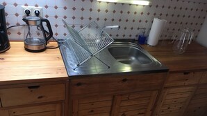 A kitchen with a stainless steel sink, wooden cabinets, a kettle, and a dish rack. - Chickes apartment in perfect location (Graz)