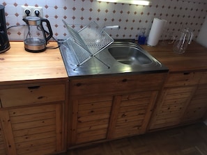 A kitchen with a stainless steel sink, wooden cabinets, a kettle, and a dish rack. - Chickes apartment in perfect location (Graz)