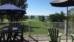 Eine Terrasse mit Sitzgelegenheiten, Blick auf einen Golfplatz und ein Gewässer in der Ferne.