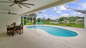 A swimming pool with a curved edge, a dining table with chairs, and ceiling fans. - Rovigo Vacation Rental: Spacious Retreat with Panoramic Lake Views in Kings Lake. 4-BR, 4-Bathroom Home with Private Pool, just 3.4 Miles from the Vibrant Fifth Avenue South and Naples Attractions (Naples)