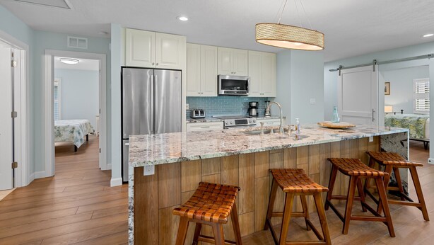 A modern kitchen with a large island, stainless steel appliances, and wooden bar stools. - Rovigo Vacation Rental: Spacious Retreat with Panoramic Lake Views in Kings Lake. 4-BR, 4-Bathroom Home with Private Pool, just 3.4 Miles from the Vibrant Fifth Avenue South and Naples Attractions (Naples)