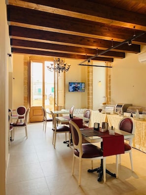 A dining area with a wooden ceiling, a chandelier, a television mounted on the wall, and a buffet setup. - Castello Castriota Scanderbeg Suites De Charme (Galatina)