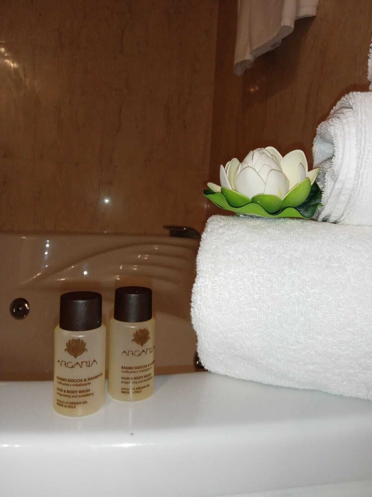 A bathroom with a bathtub, two bottles of Argania hair and body wash, and a white towel with a lotus decoration.