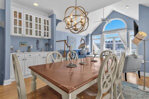 A dining area with a wooden table, white chairs, a chandelier, and a view of the outside.