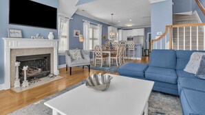 Un salon avec une cheminée, un canapé bleu, une table à manger et un escalier.