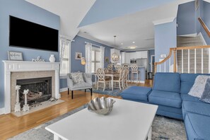 A living room with a fireplace, a blue sofa, a dining table, and a staircase.