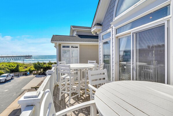 A balcony with white furniture, a view of the ocean, and a pier in the background.