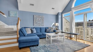 A living room with a blue sofa, a white coffee table, and a large window with a view of the outside.
