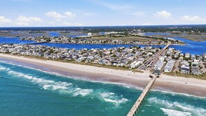 Une vue aérienne d’une ville côtière avec une longue jetée qui s’avance dans l’océan, entourée de bâtiments résidentiels et d’une plage.