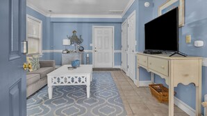 A living room with a white coffee table, a sofa, a TV on a stand, and a patterned rug.