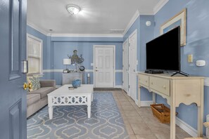 A living room with a white coffee table, a sofa, a TV on a stand, and a patterned rug.