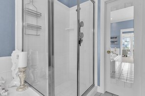 A modern bathroom with a glass shower enclosure, white tiled walls, and a visible sink area.
