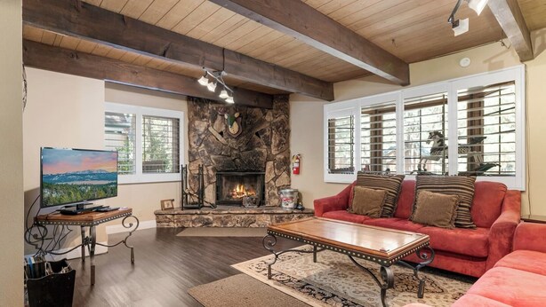 A cozy living room with a stone fireplace, a red sofa, a wooden coffee table, and a television on a stand.
