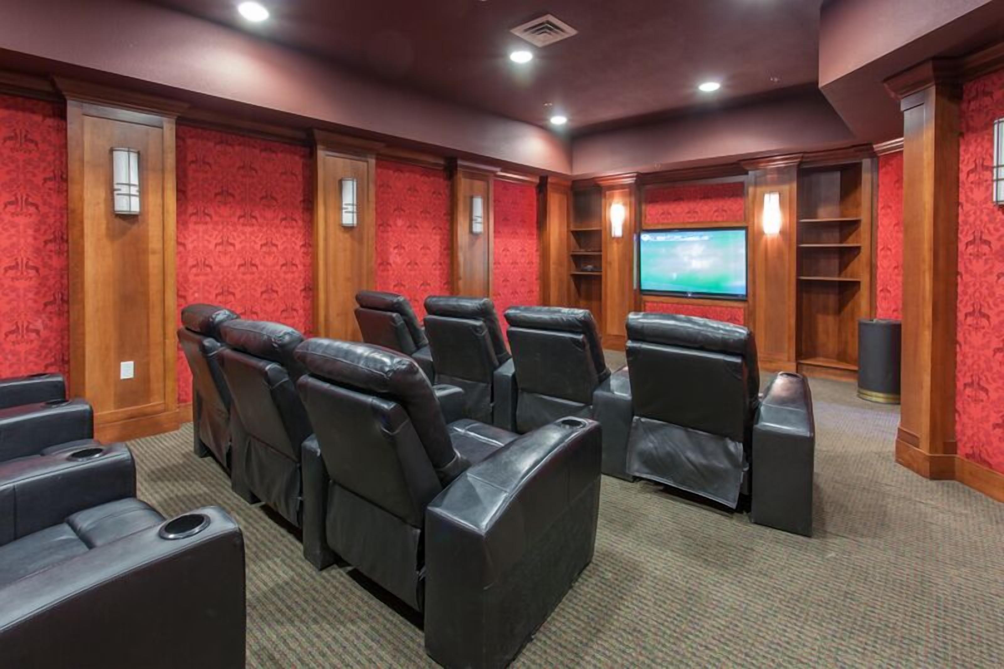 Una sala de cine en casa con sillones reclinables de cuero, una pantalla grande y paneles de madera.