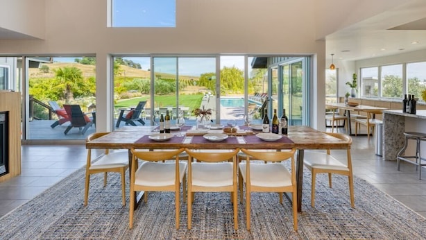 A modern dining area with a large table and chairs, large windows, and a view of a pool and garden. - Private Sonoma Vineyard Estate: Modern Villa + Pool 10 Acre Winery Property (Sonoma)