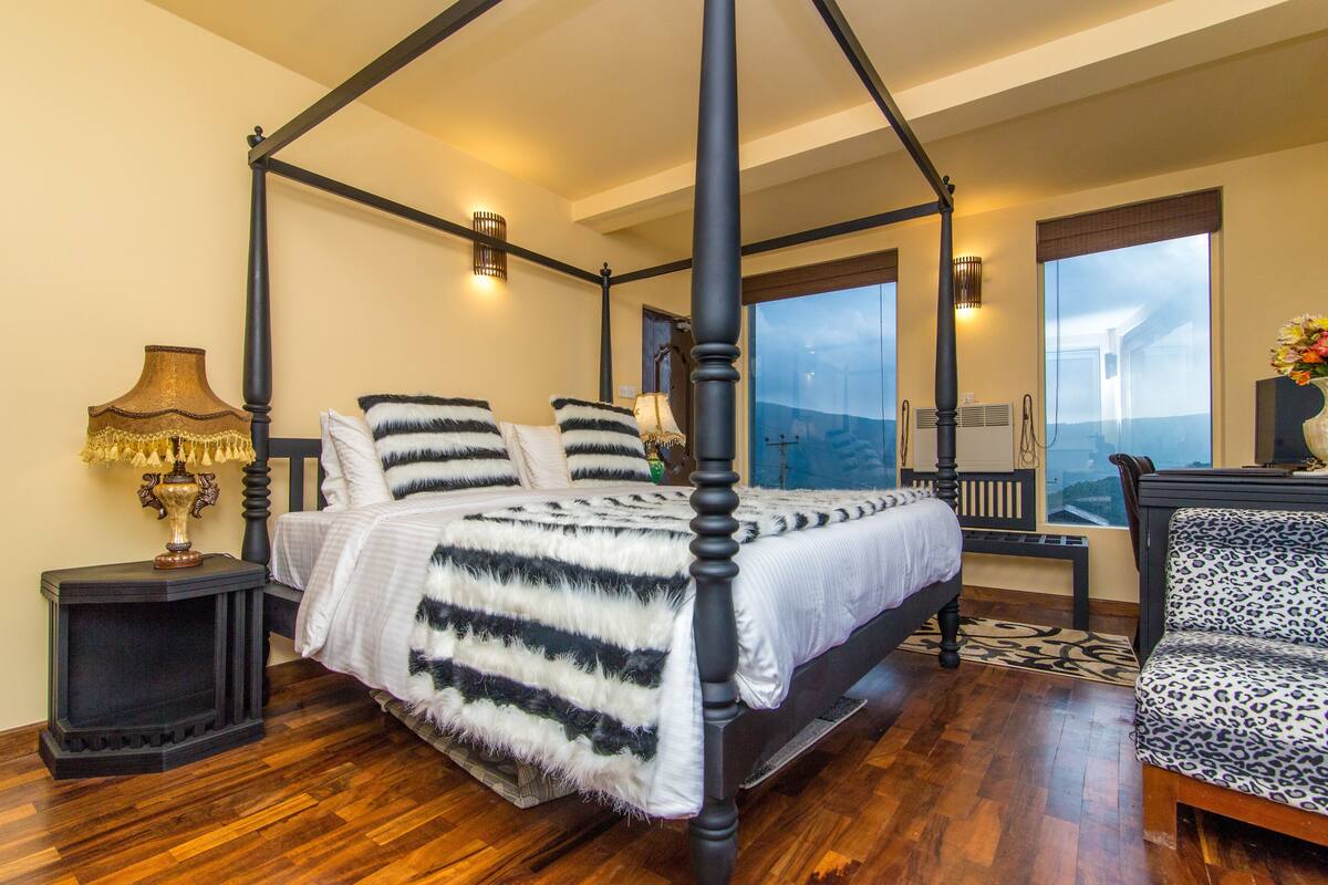 A four-poster bed with a white and black striped bedspread, a black nightstand with a lamp, and a leopard print chair.