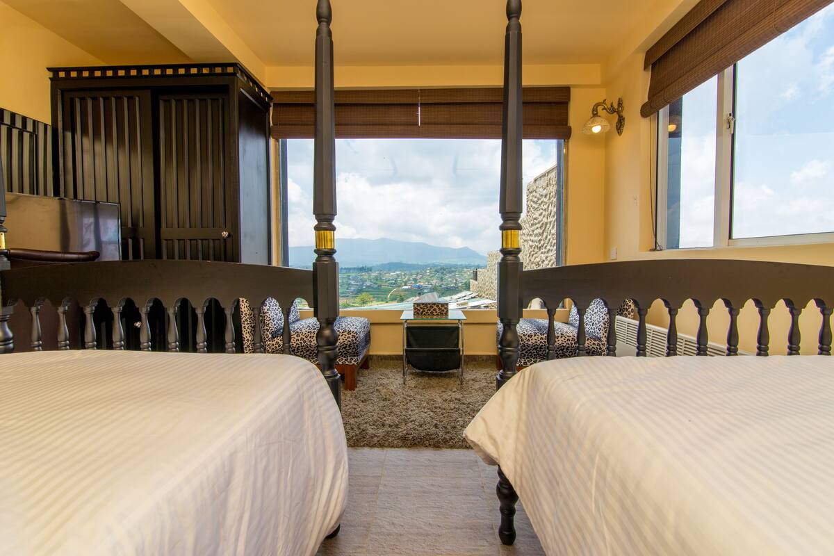 A bedroom with two beds, a small table, and a view of the landscape.