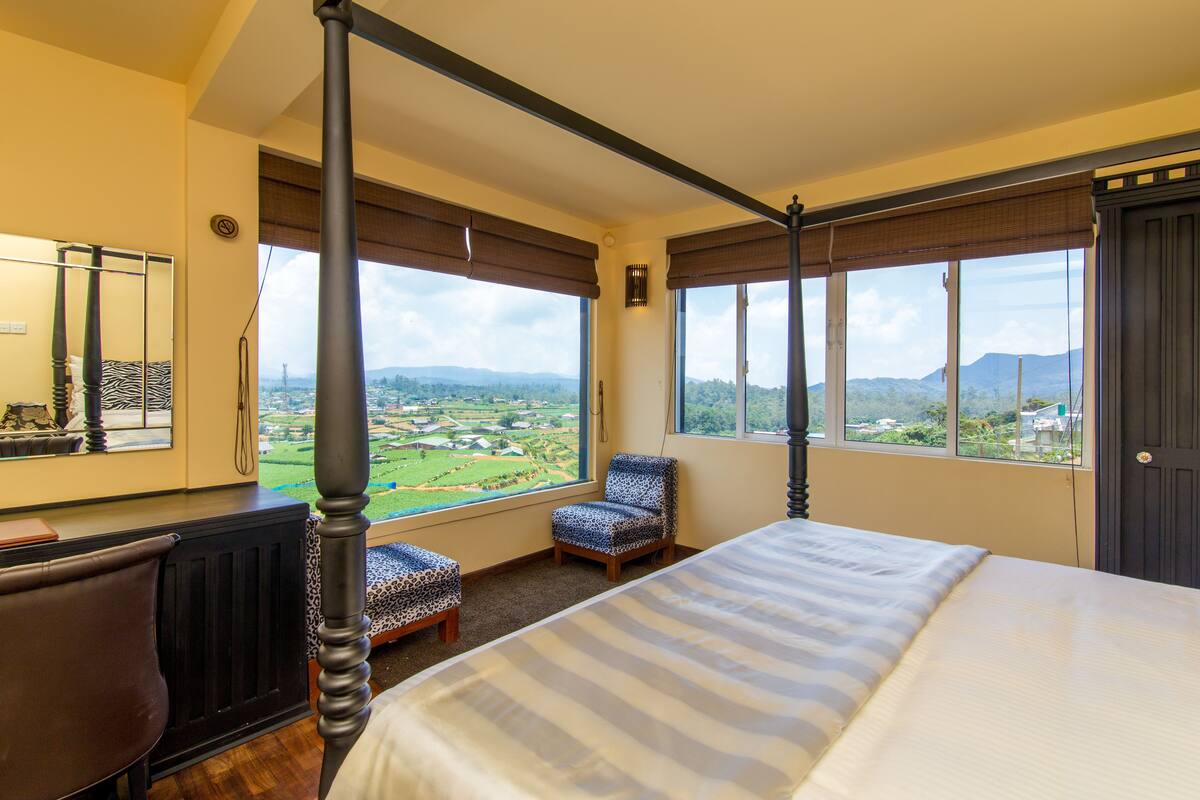 A four-poster bed with a view of a green landscape through large windows.