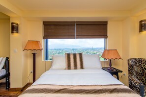 A hotel room with a large bed, two bedside lamps, a leopard print chair, and a window with a city view. - The Forest and lake by Schofieldshire (Nuwara Eliya)