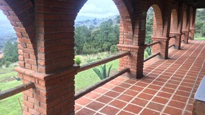 A covered terrace with brick arches and a tiled floor, overlooking a lush landscape.