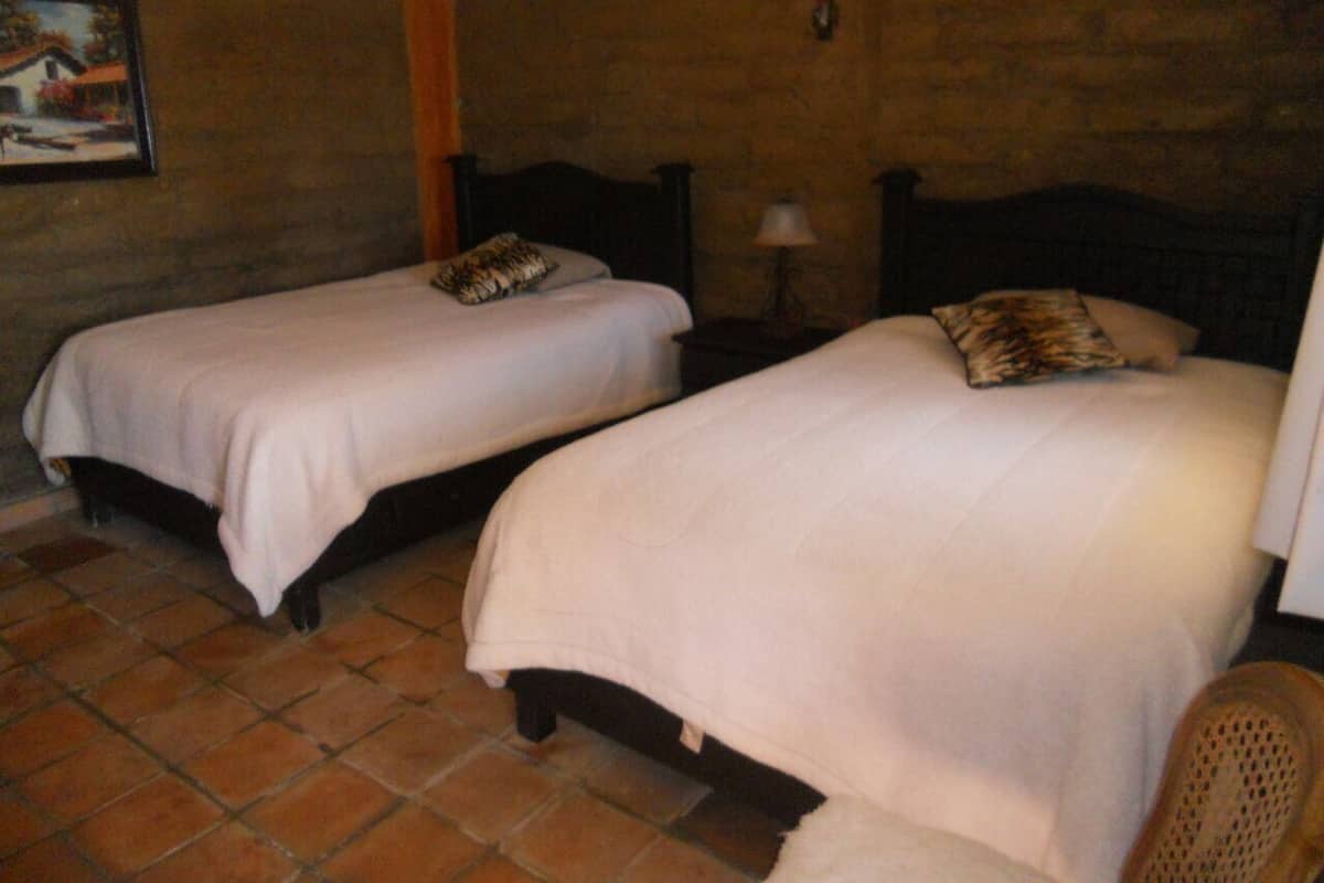 Two single beds with headboards, a lamp, and a chair in a room with tiled flooring and a brick wall.