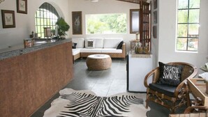 A spacious living area with a sofa, a zebra-patterned rug, a wooden chair, and a kitchen area with a counter and a refrigerator. - Hotel Fazenda Reviver (Araçoiaba da Serra)