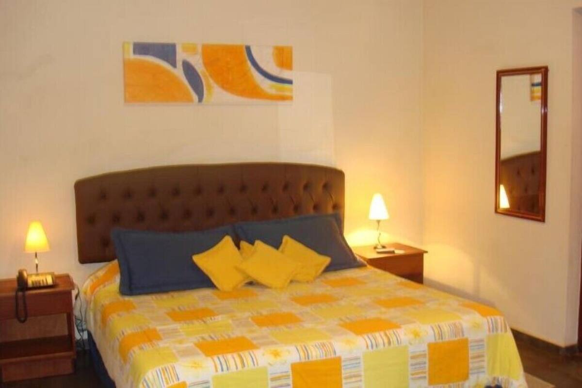 Un dormitorio con una cama, dos mesitas de noche, un tocador, un espejo colgado en la pared y una obra de arte abstracta.