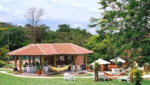 A covered outdoor seating area with tables and chairs, surrounded by greenery and trees. - Hotel Fazenda Reviver (Araçoiaba da Serra)