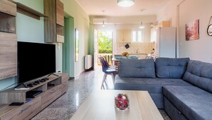 A modern living room with a flat-screen TV, grey sofa, and wooden entertainment unit. - Riposo Studios & Apartments (Corfu)