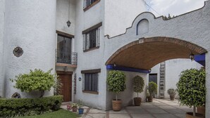 Un patio con un edificio blanco, un camino de ladrillo y plantas en macetas.