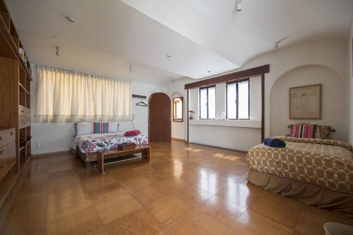 Un dormitorio amplio con piso de madera, una cama grande con ropa de cama estampada, un armario y una ventana con cortinas.