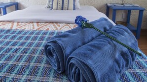Una cama bien hecha con una colcha estampada y una toalla enrollada, una almohada con diseño azul y blanco, y un cuadro colgado en la pared.