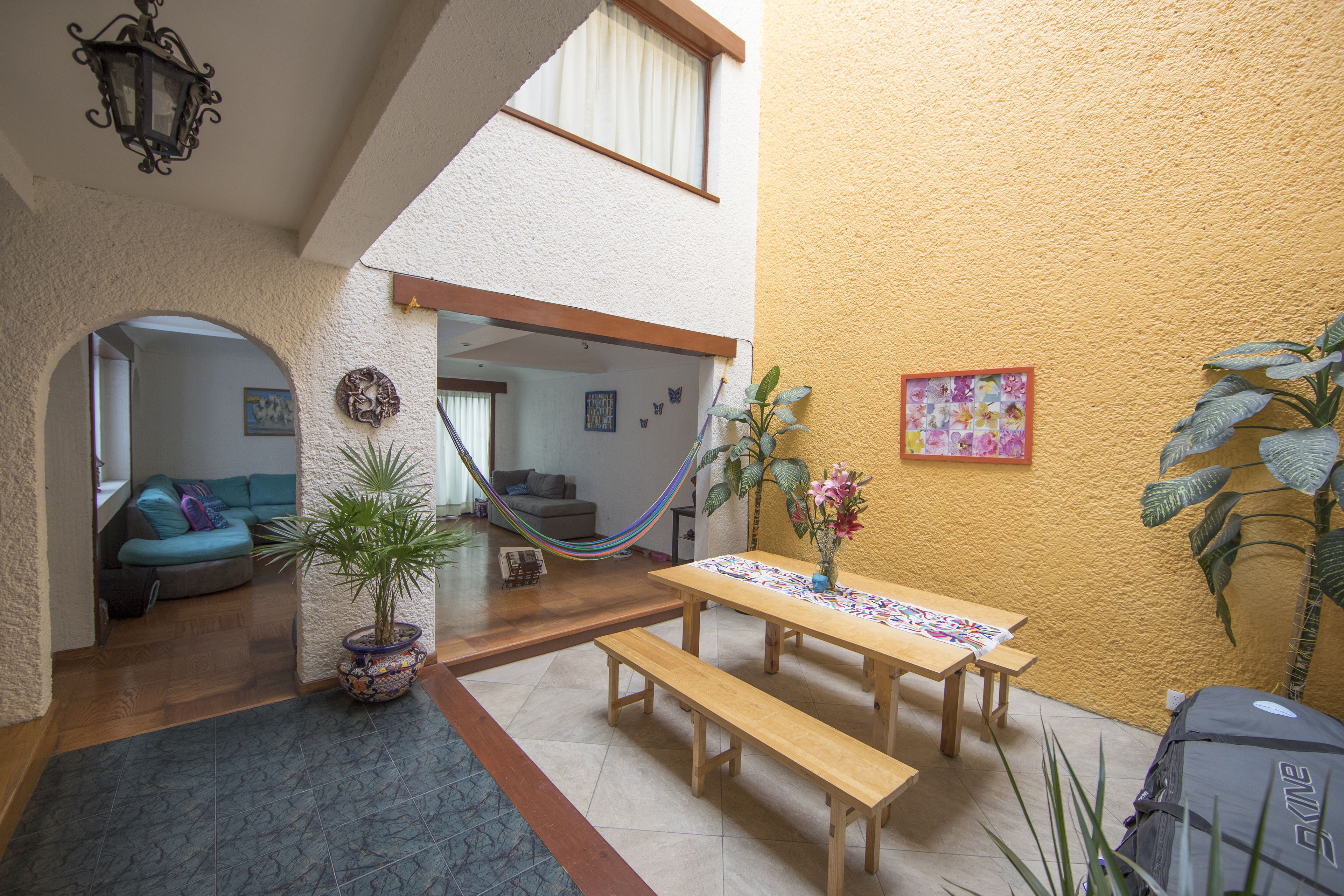Un espacio interior acogedor con una mesa de madera y bancos, una hamaca y una planta en maceta.